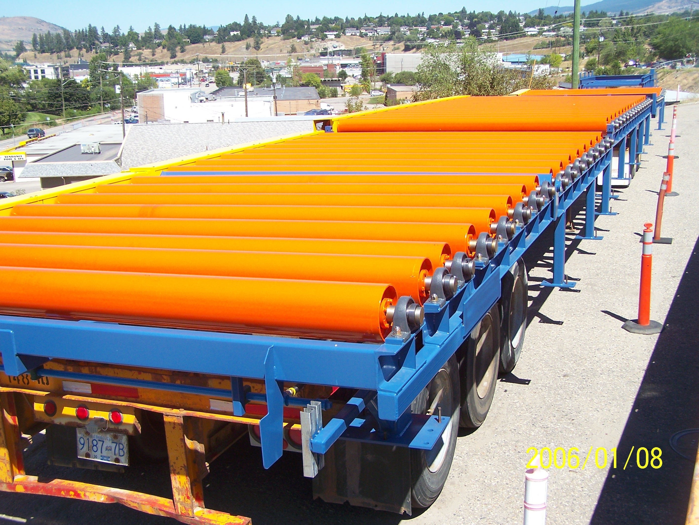 Orange industrial conveyor rollers on a blue flatbed truck with scenic city background. Orange industrial conveyor rollers on a blue flatbed truck with scenic city background.
